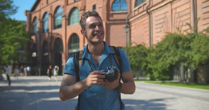 Medium shot of young caucasian tourist man smiling happy using vintage camera at city.