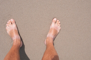Tanned bare men's feet on  sand of a beach