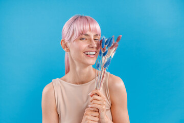 Lovely woman with pink hair smiling at camera, holding dried pampas grass in her hand, posing over...