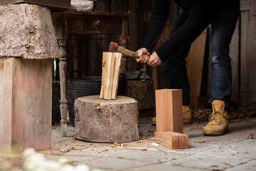 Lumberjack man splitting logs of wood with an old axe on a big wooden stump to use for his fire wood stove while being self sufficient and living the simple life