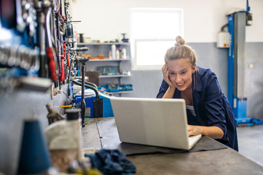 Business woman at a factory. Craftswoman working using a laptop in the garage. Mechanic using laptop at the repair garage. Young female mechanic with laptop. Business woman at a factory. - Powered by Adobe