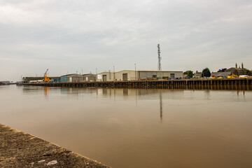 Fototapeta na wymiar Industrial units on the edge of the River Yare on a cloudy and dull day. Great Yarmouth, July 2021.