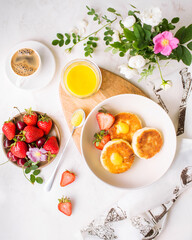 Summer breakfast with fresh berries. Cheesecakes with mango sauce and strawberries. Freshly brewed espresso coffee on a white background. Beautiful breakfast serving. Serving food with flowers