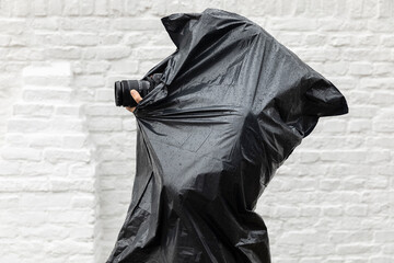 Photographer photographing in the rain while wearing a plastic black waterproof barbage bag as a poncho to protect herself from the bad wet cold weather. Dedication concept