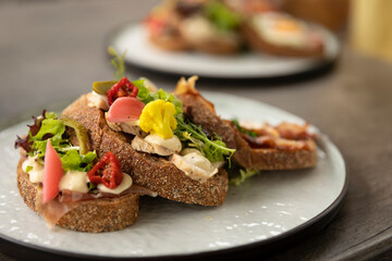 Healthy homemade club sandwich dish with fresh ingredients such as tomato, salad, lettuce, bacon, cauliflower and chicken on a rustic brown bread beautifully presented on a plate on a terrace