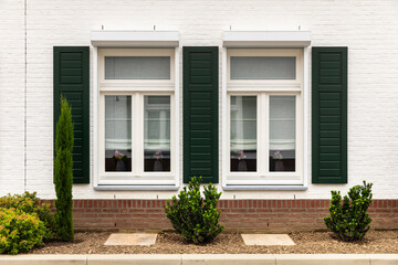 Fototapeta na wymiar Symmetrical facade of a white modern house with an orange roof in Thorn, The Netherlands, known for its white houses and buildings. Green shutters next to the windows, greenery and plants
