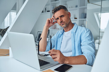 Naklejka premium Confident mature man looking at camera while sitting at the office desk