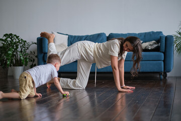 Happy mindful single mother doing morning exercises in yoga pose with kid playing at home. morning...