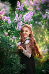 Portrait of a cute schoolgirl in a school uniform among lilacs in spring
