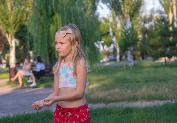 little girl, blonde, 7 years old, plays in the park, holds sand in her hands