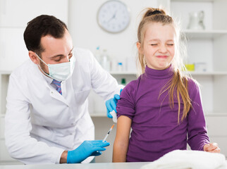 Smiling man doctor making injection to little girl patient in hospital