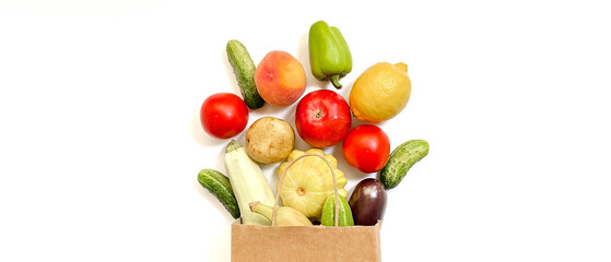 A paper shopping bag from which vegetables and fruits fall out, namely tomato, cucumber, squash, pepper, lemon, eggplant, zucchini, banana, apple, peach on white background.