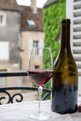 Tasting of burgundy red wine from grand cru pinot noir  vineyards, glass and bottle of wine and view on old town street in Burgundy wine region, France
