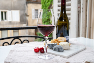 Tasting of burgundy red wine from grand cru pinot noir  vineyards with french goat cheeses and view on old town street in Burgundy wine region, France