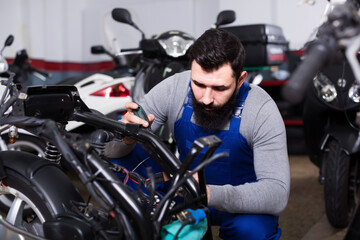 Fototapeta na wymiar Positive male worker repairing failed scooter in motorcycle workshop
