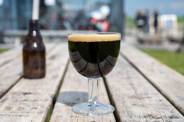 Glass of dark strong belgian beer served on outdoor terrace with green grass meadow on background