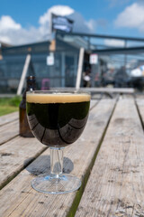 Glass of dark strong belgian beer served on outdoor terrace with green grass meadow on background