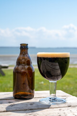 Glass of dark strong belgian beer served on outdoor terrace with green grass meadow on background