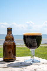 Glass of dark strong belgian beer served on outdoor terrace with green grass meadow on background