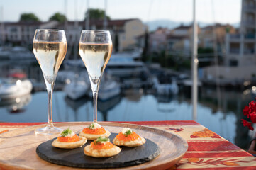 Russian style party with two glasses of white cold champagne, bliny with red caviar and view on Port Grimaud near Saint-Tropez in summer