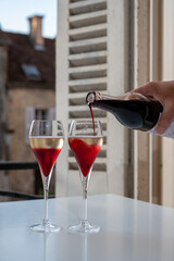 Drinking of Kir Royal,  French aperitif cocktail made  from creme de cassis topped with champagne, typically served in flute glass, with view on old French village