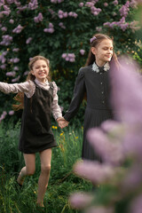 Obraz premium Two cute schoolgirls in school uniform among lilacs in spring