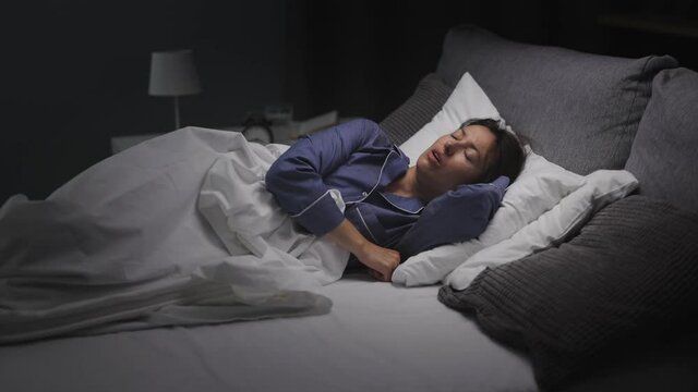Caucasian female with dark hair lying in bed and having sleeping problems. Mature stressed woman in pajamas suffering from insomnia at night.