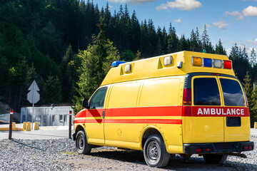 Fototapeta na wymiar Side view of yellow ambulance rescue ems van car parked near countryside rural road at highland mountain resort area. Paramedic first aid help service vehicle against alpine forest landscape
