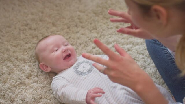 Loving mother playing game and tickling baby son lying on rug in child's bedroom at home - shot in slow motion
