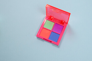 Purple, green, orange and blue eye shadow palette isolated on a blue background. Make up. Neon colours.