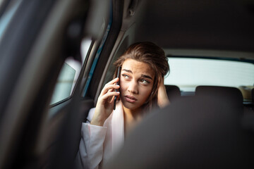 Sad young woman looking through the car window. Bored woman in a car talking on smartphone. Pensive woman looking out of a car window. Sad young woman in the car