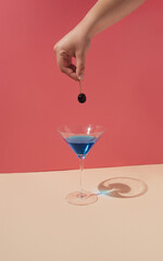 Womans hand holding cherry above martini glass. Minimal party concept.