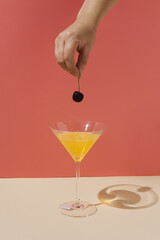 Womans hand holding cherry above martini glass full of orange juice. Minimal party concept.