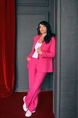 Beautiful trendy actress woman entertainer in pink suit on red velvet curtains background. Theater,...