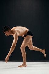 Fototapeta na wymiar man bodybuilder in black shorts bent knees dark background