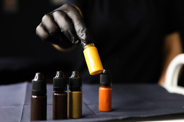 the hand of the master of permanent makeup to raise the yellow pigment for tattoos with your fingers