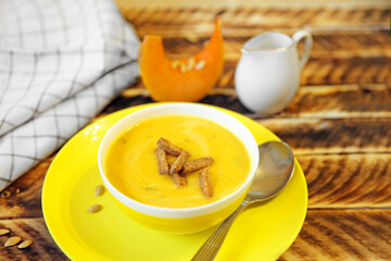 Pumpkin soup in a yellow plate on a wooden background.