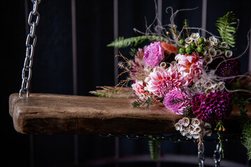 On a wooden board swing lies wedding bouquet suspended on iron chains in a cage in dark loft...