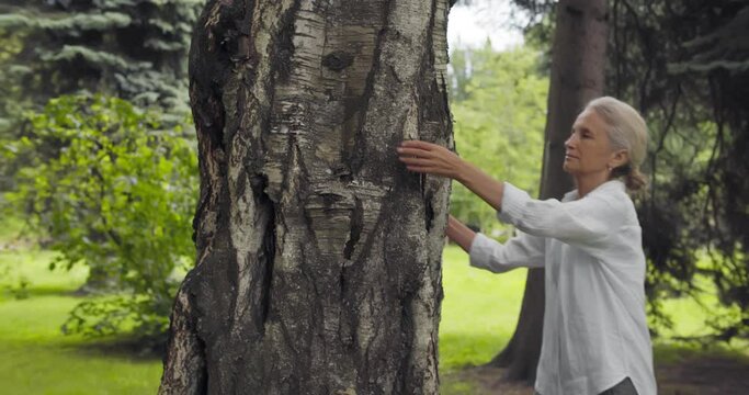 Side view of mature woman hugging tree and smiling outdoor.