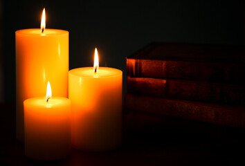 Three Pillar Candles Burning in a Dark Room with a Stack of Antique Books