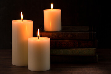 Three Pillar Candles Burning in a Dark Room with a Stack of Antique Books