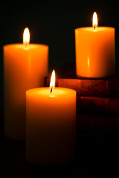 Three Pillar Candles Burning in a Dark Room with a Stack of Antique Books
