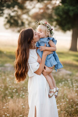 Young mother kissing her little daughter in the park on summer day. Family holiday in garden....
