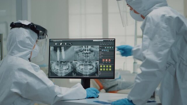 Team of stomatologists analyzing dental x ray scan on computer monitor at oral care clinic. Caucasian orthodontists examining teeth radiography with modern technology for implant
