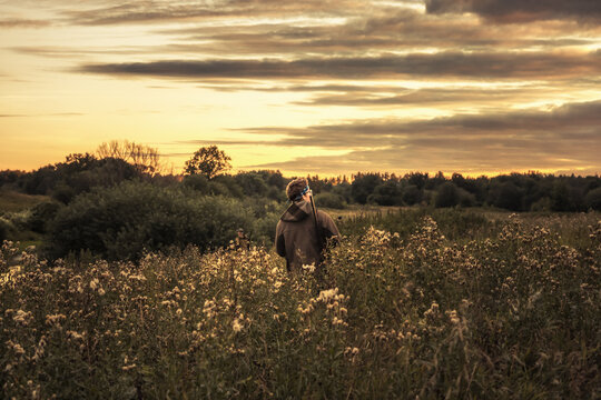 Hunter man standing alone in rural field during hunting and looking into the distance at beautiful sunset 