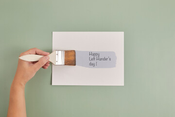 Happy Left Hander's Day. Left hand hold brush and writing text.