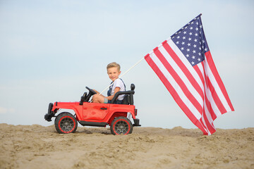 A boy with an American flag in a small toy car.
