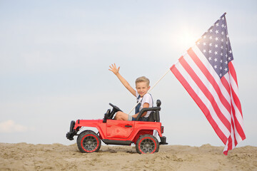 A boy with an American flag in a small toy car.