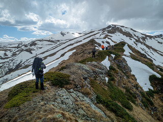 A group of tourists with backpacks moves along a mountain range, partially covered with snow. Hiking in the mountains. Mountain landscape.