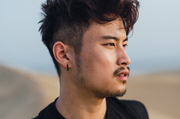 Fototapeta premium Portrait of young handsome Chinese tourist standing while admiring the sand dunes in Maspalomas